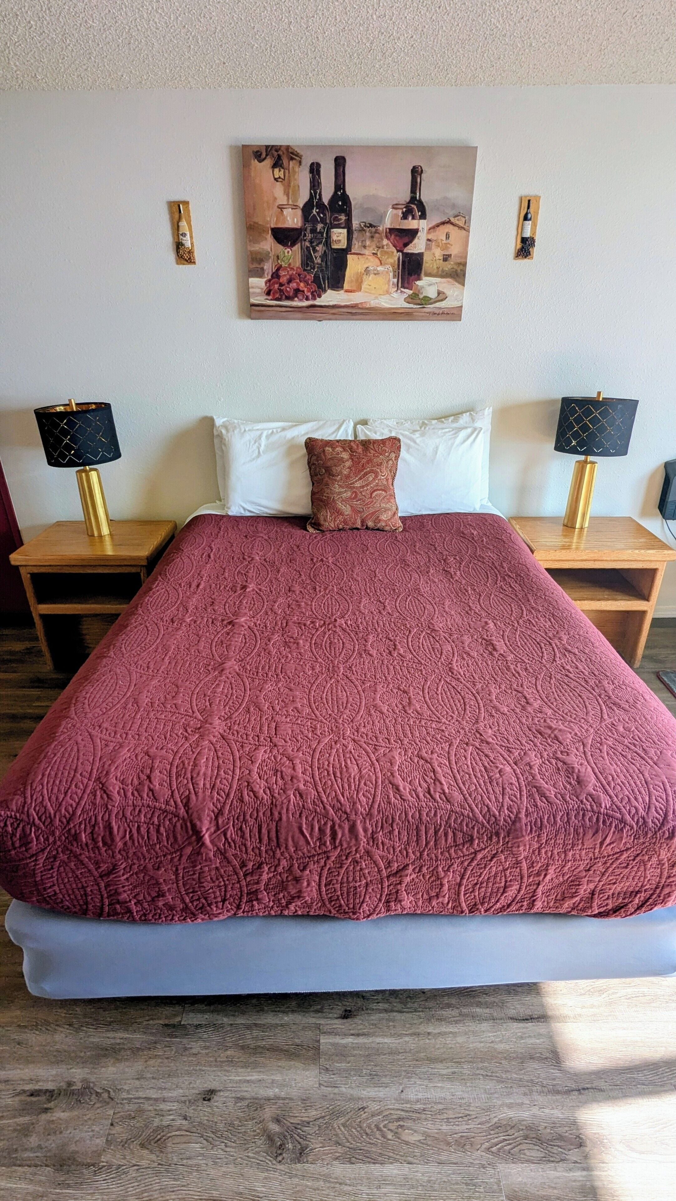 A bedroom with a large bed, a painting on the wall, and two bedside tables with lamps.