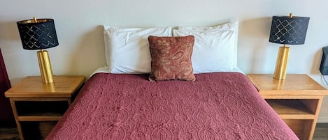 A bedroom with a large bed, a painting on the wall, and two bedside tables with lamps.
