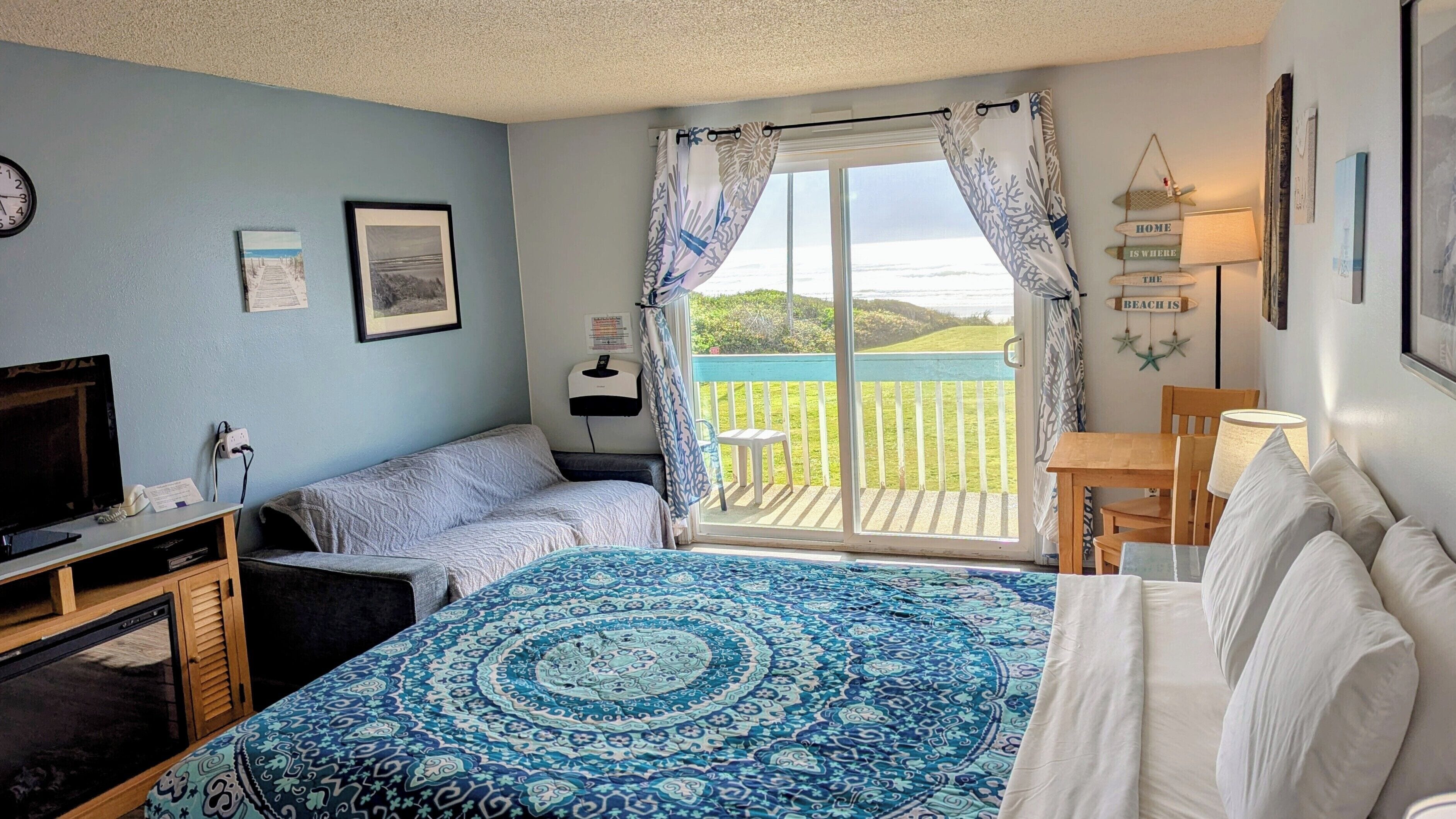 Un dormitorio con cama, televisión, escritorio, silla y balcón con vistas a la playa.