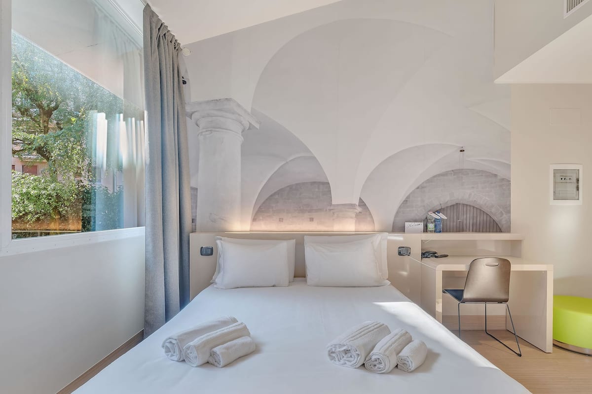 Ein Hotelzimmer mit einem Bett, einem Schreibtisch und einem Stuhl. Auf dem Bett liegen Handtücher.