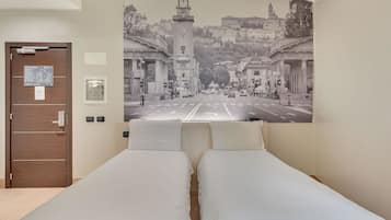 Camera d'albergo con un grande murale raffigurante un panorama urbano, due letti singoli, una porta in legno e una piccola finestra.