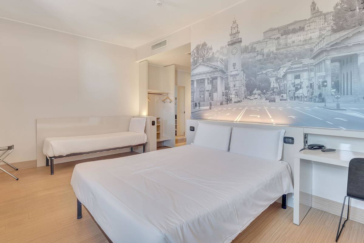 Ein Hotelzimmer mit Bett, Schreibtisch und einem großen Fenster mit Blick auf die Stadt.