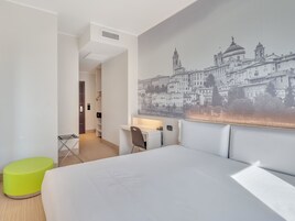 Una camera d'albergo moderna con un letto grande, una scrivania e una sedia verde brillante.