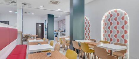 A modern dining area with booths and tables, a kitchen in the background, and patterned walls.