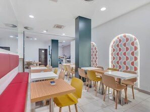 A modern dining area with booths and tables, a kitchen in the background, and patterned walls. - B&B HOTEL Bergamo City (Bergamo)