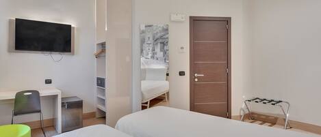 A modern hotel room with a bed, a desk, a chair, a wardrobe, and a TV.