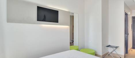 Quarto de hotel moderno com uma cama grande, uma televisão de tela plana na parede, um banquinho verde e um varal.