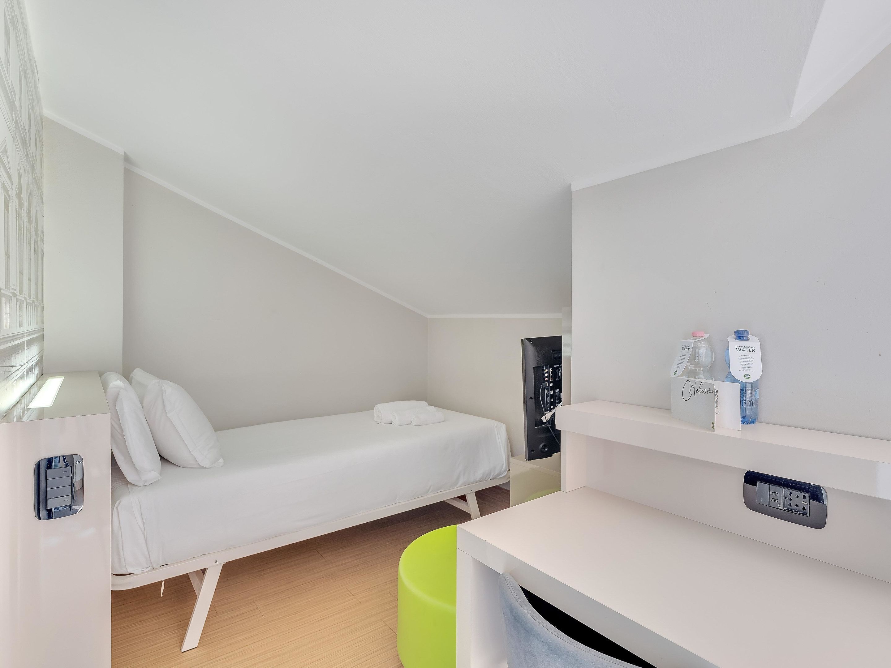 A modern, minimalistic room with a bed, a desk, and a small trash bin.