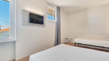 A hotel room with a bed, a TV mounted on the wall, a window with curtains, and a small table with a lamp.