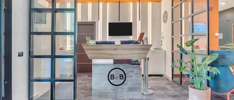 A hotel reception area with a wooden reception desk, a large potted plant, and a modern interior design.