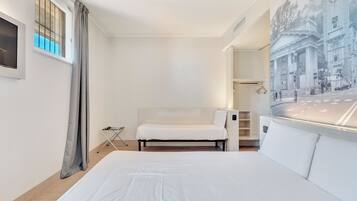 Habitació d'hotel moderna amb un llit gran, una zona de seients petita, una finestra amb cortines i vista a un paisatge urbà a través d'una finestra ampla.