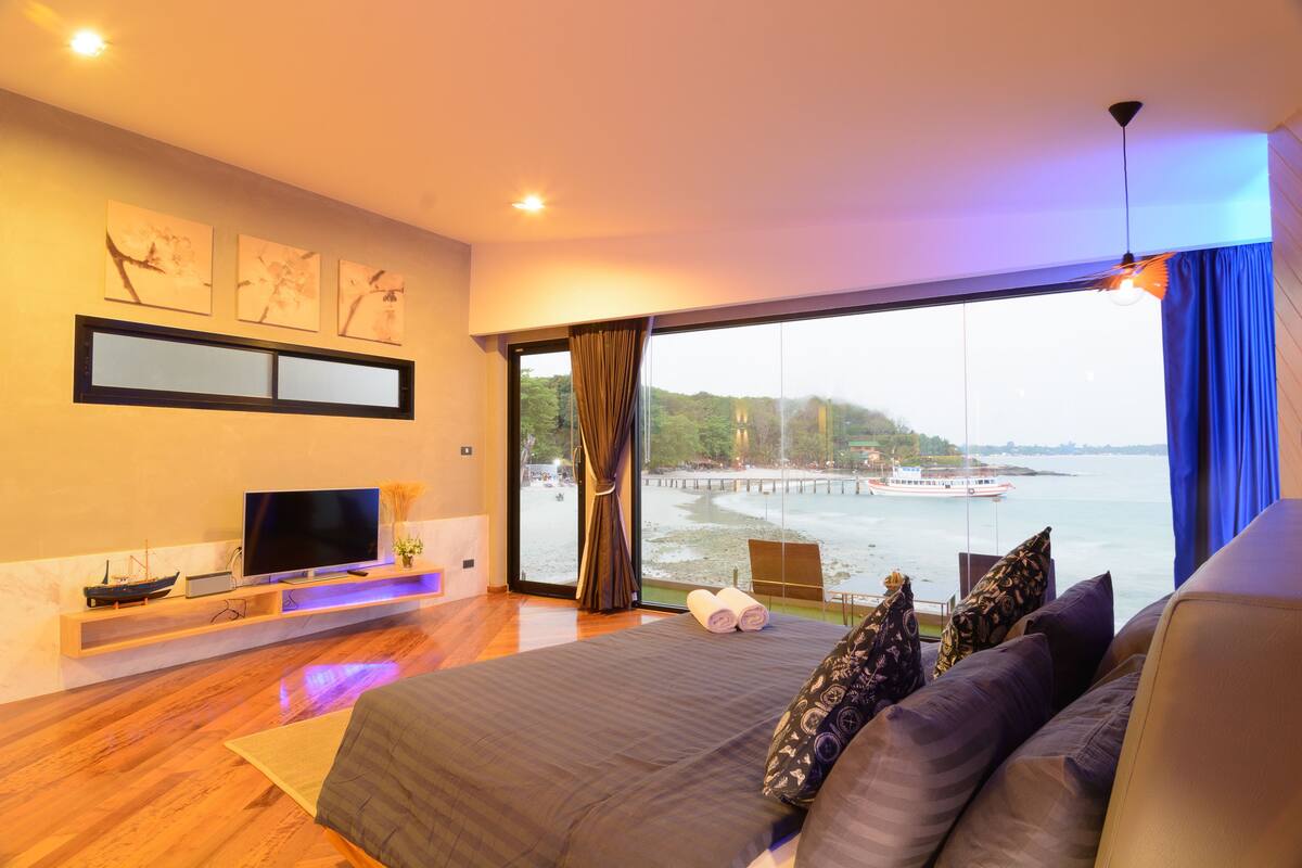 Ein modernes Schlafzimmer mit einem großen Bett, einem Flachbildfernseher, Kunstwerken an der Wand und Blick auf einen Wasserweg.