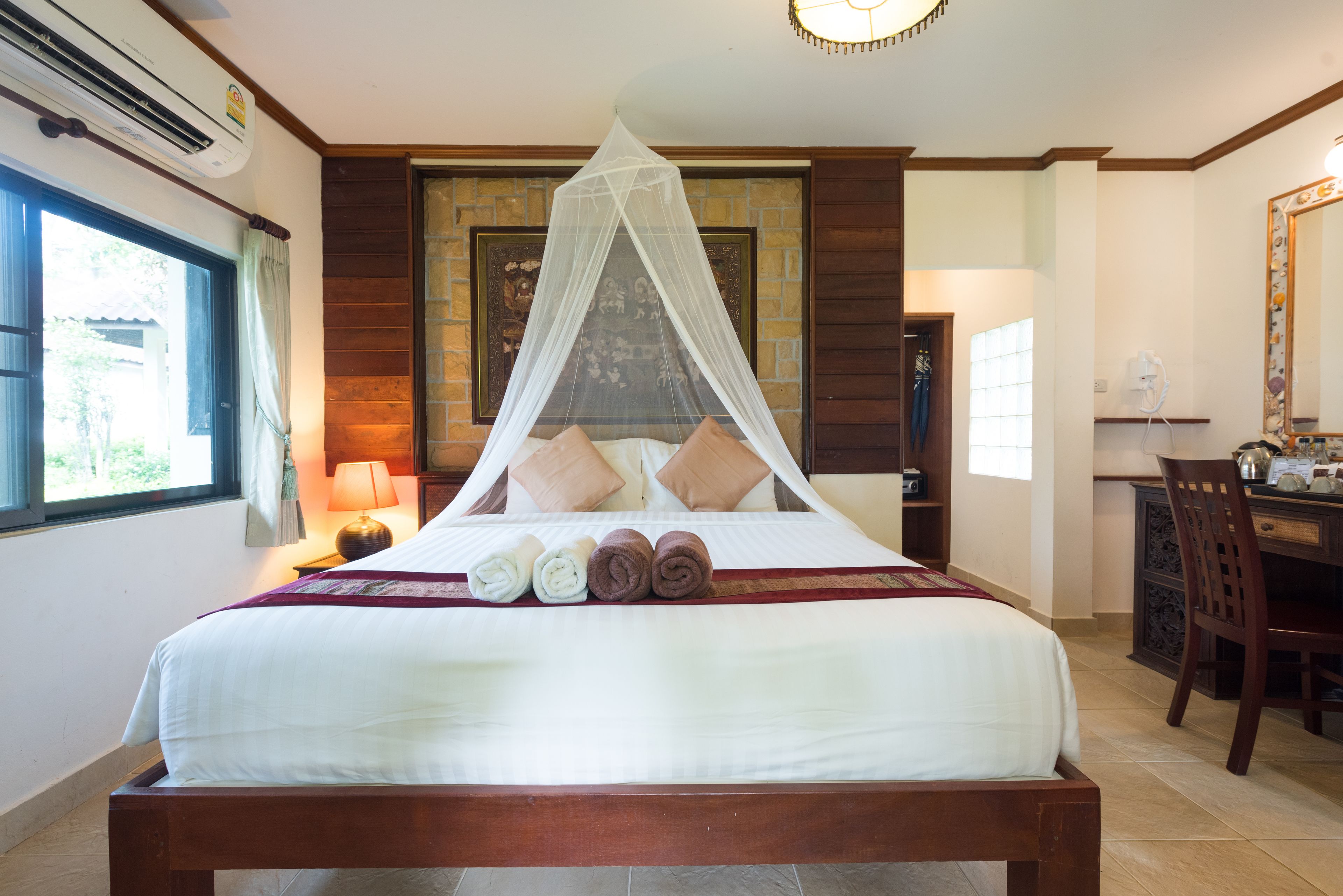 A neatly made bed with a canopy, a desk with a chair, and a window with curtains.