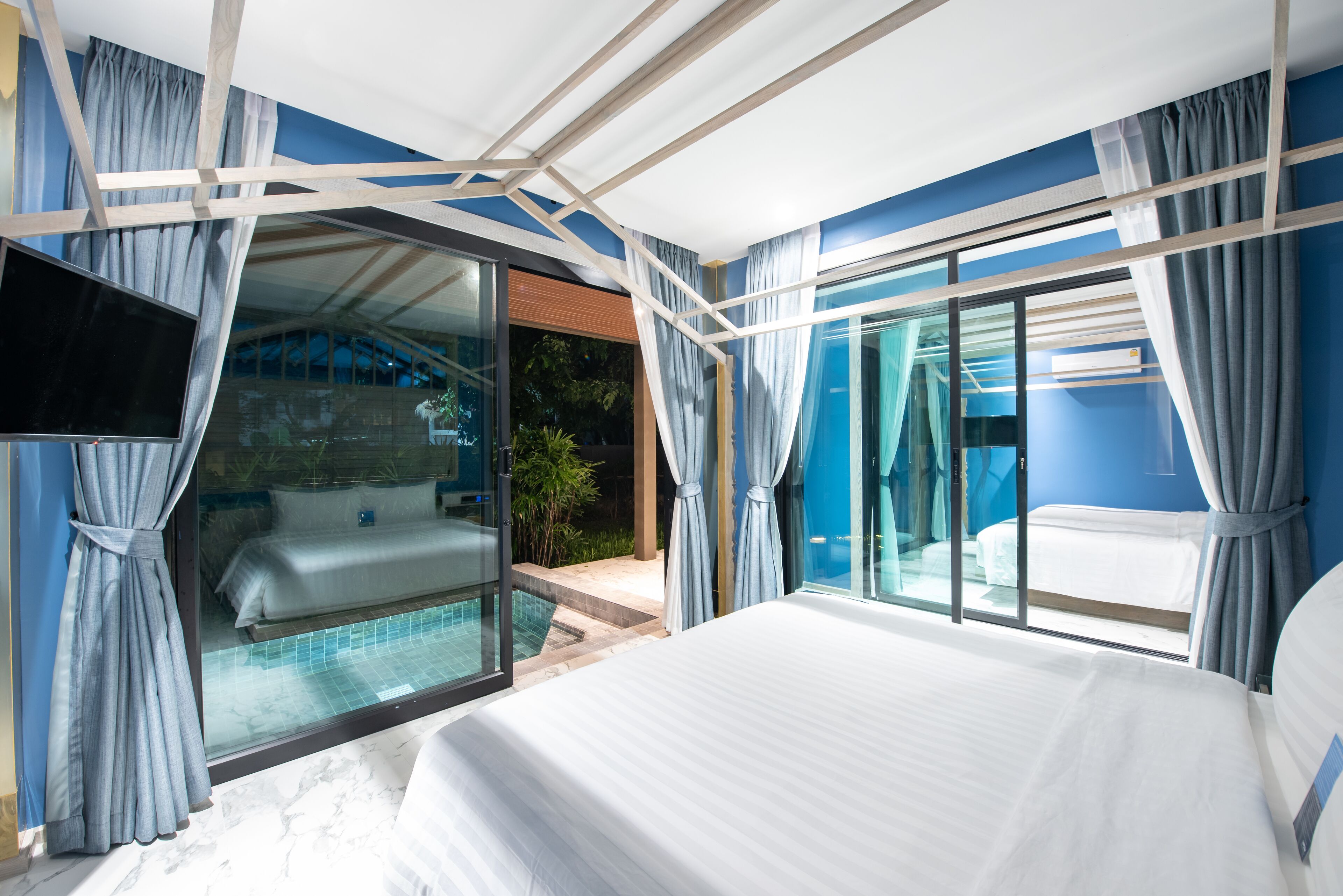 A modern hotel room with a large bed, a glass door leading to a pool, and a view of the outdoors.