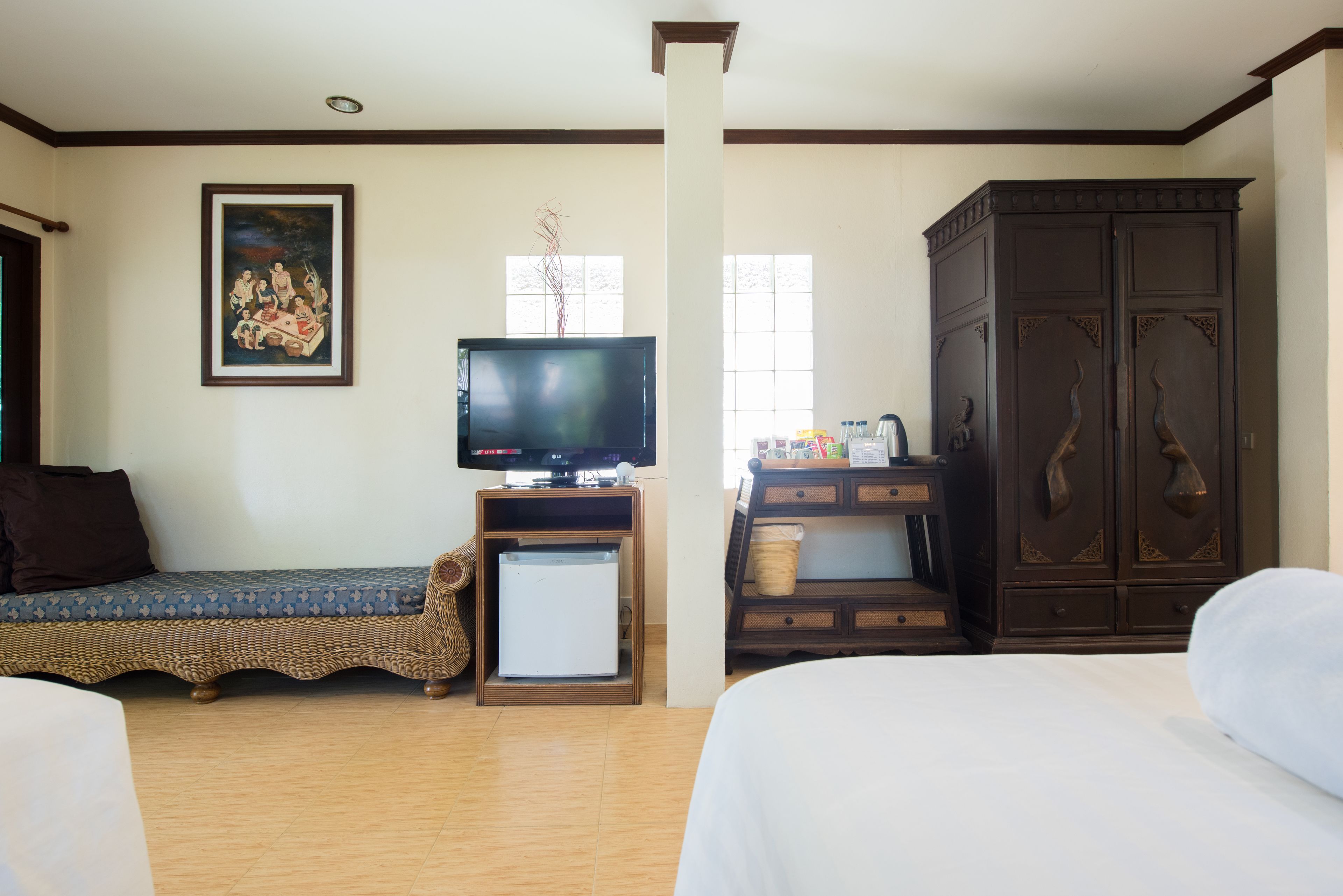 Habitación de hotel con cama, televisión, refrigerador pequeño, armario y un cuadro en la pared.