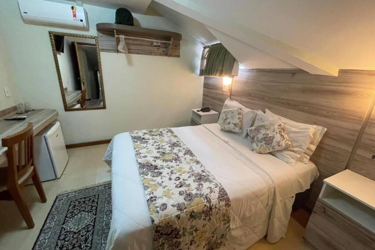 Um quarto com cama, mesa de cabeceira, abajur e escrivaninha com cadeira.