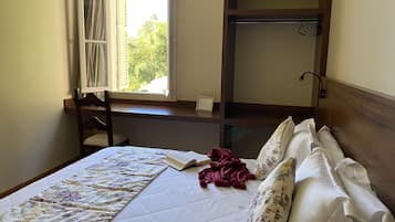 A bedroom with a bed, a window, a desk, and a wardrobe.