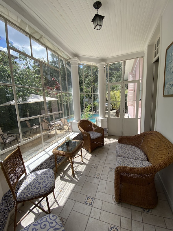 Una habitación iluminada por el sol, con ventanas amplias, mobiliario de mimbre y suelo de baldosas.