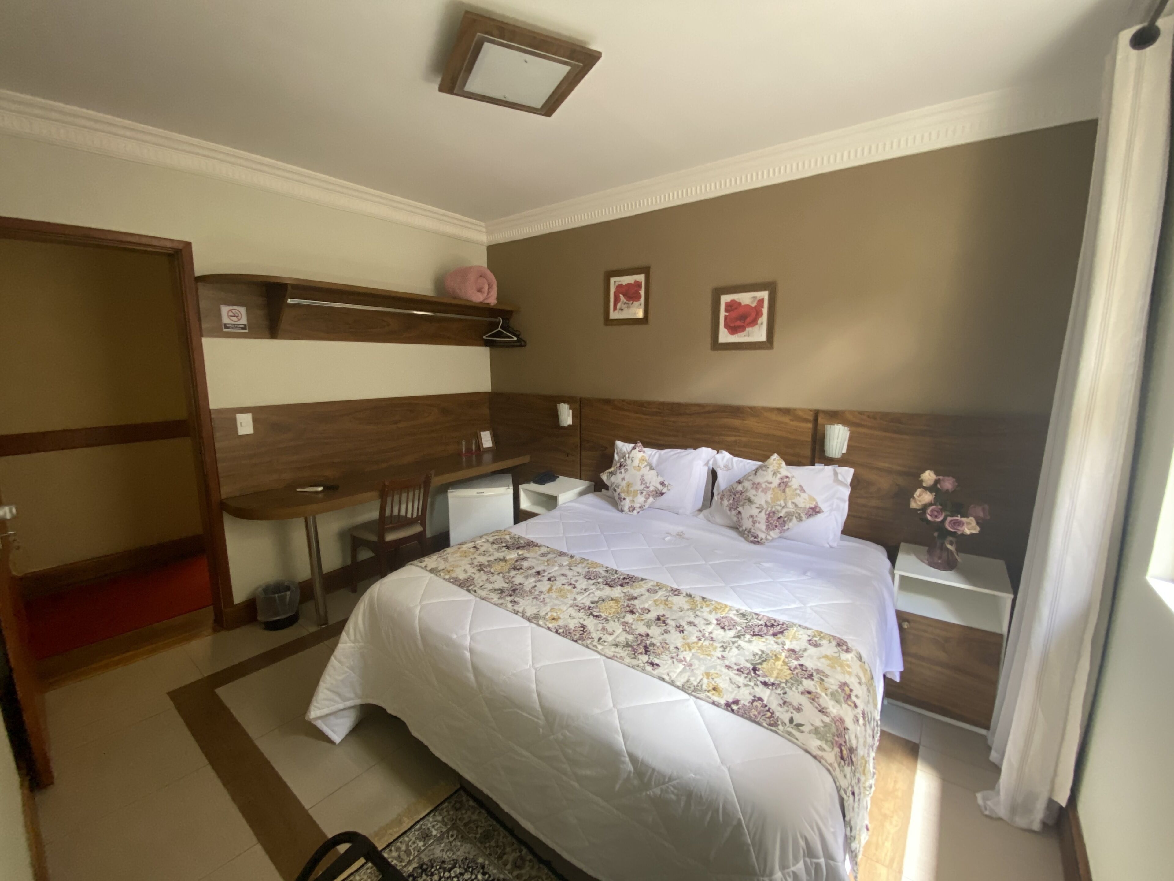 A hotel room with a bed, a desk, a chair, a nightstand, and a small table.
