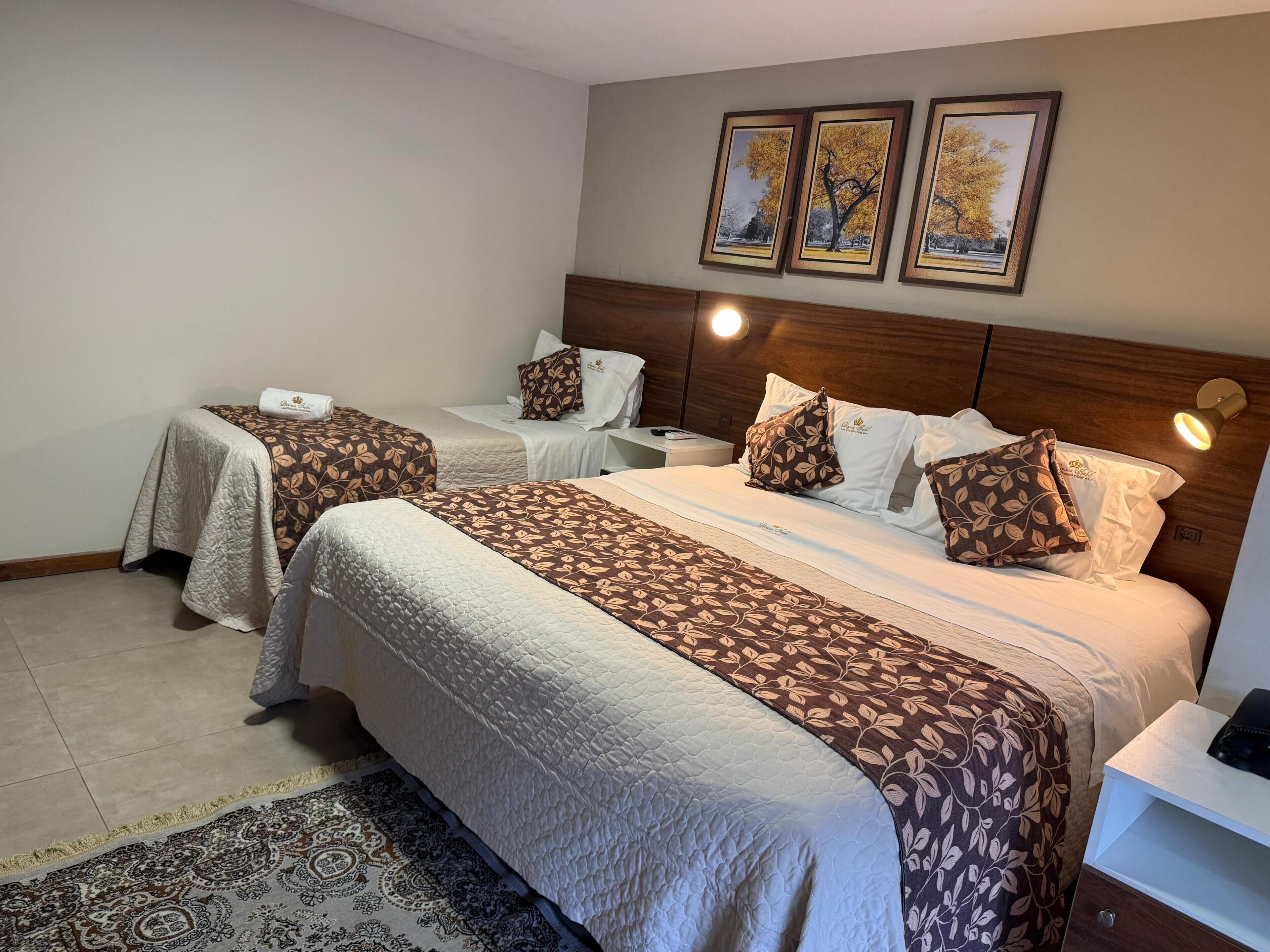 A hotel room with two beds, a nightstand, a bedside lamp, and a patterned rug.