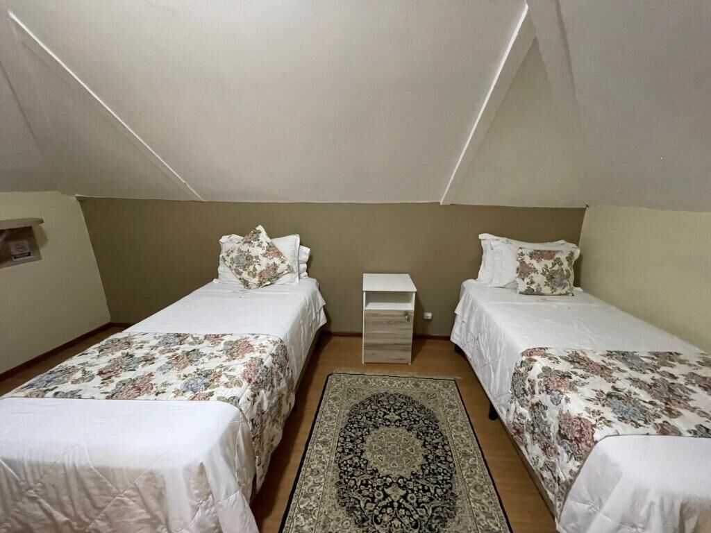 Quarto pequeno e bem iluminado com duas camas de solteiro, uma mesa de cabeceira e um tapete estampado.