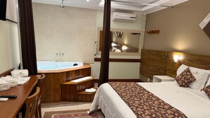 A hotel room with a large bed, a wooden desk with a chair, a bathroom with a bathtub, and a large mirror. - Pousada Princesa Isabel - Visconde (Petrópolis)