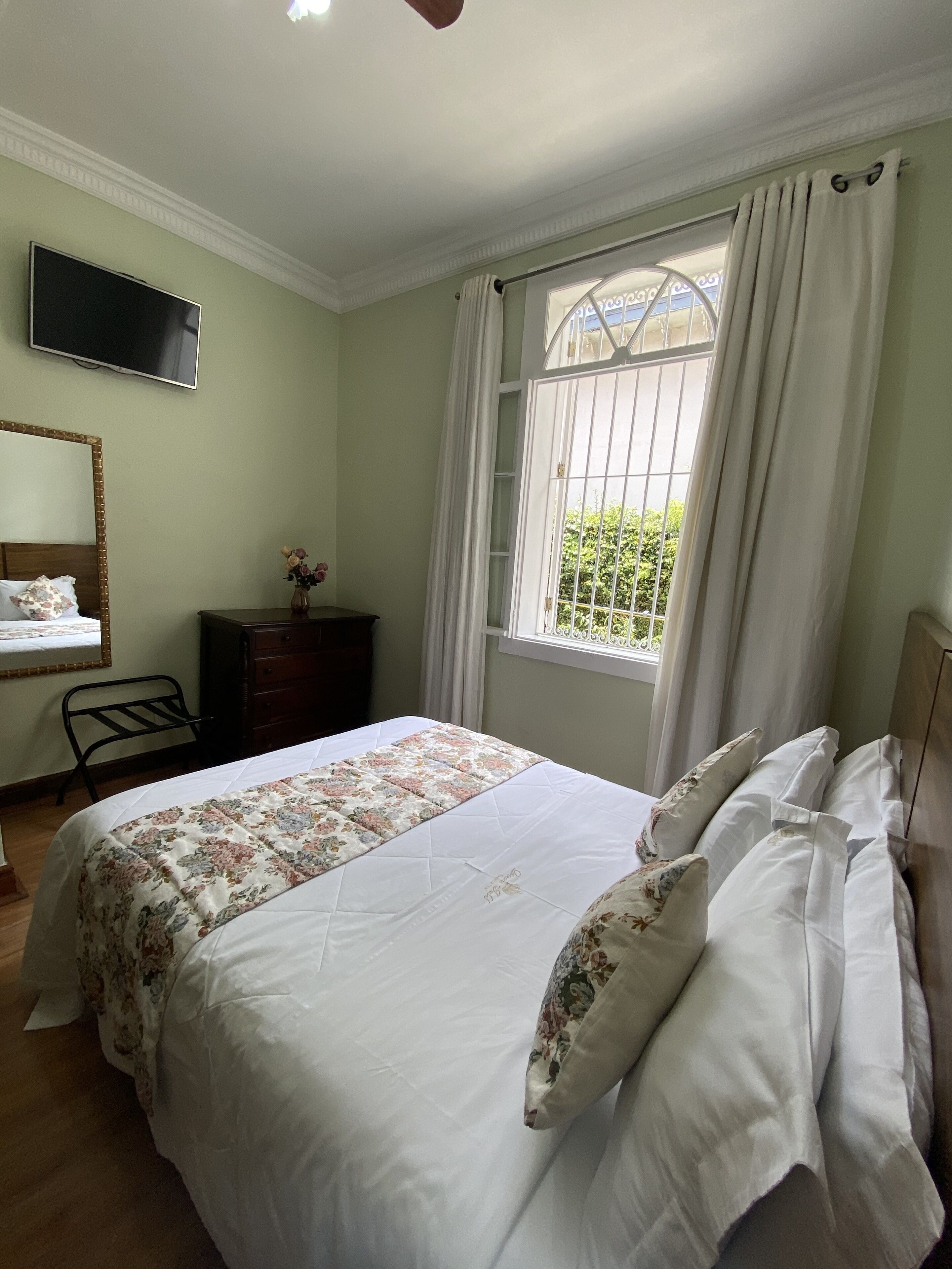 A bedroom with a bed, a dresser, a TV, and a window with curtains.