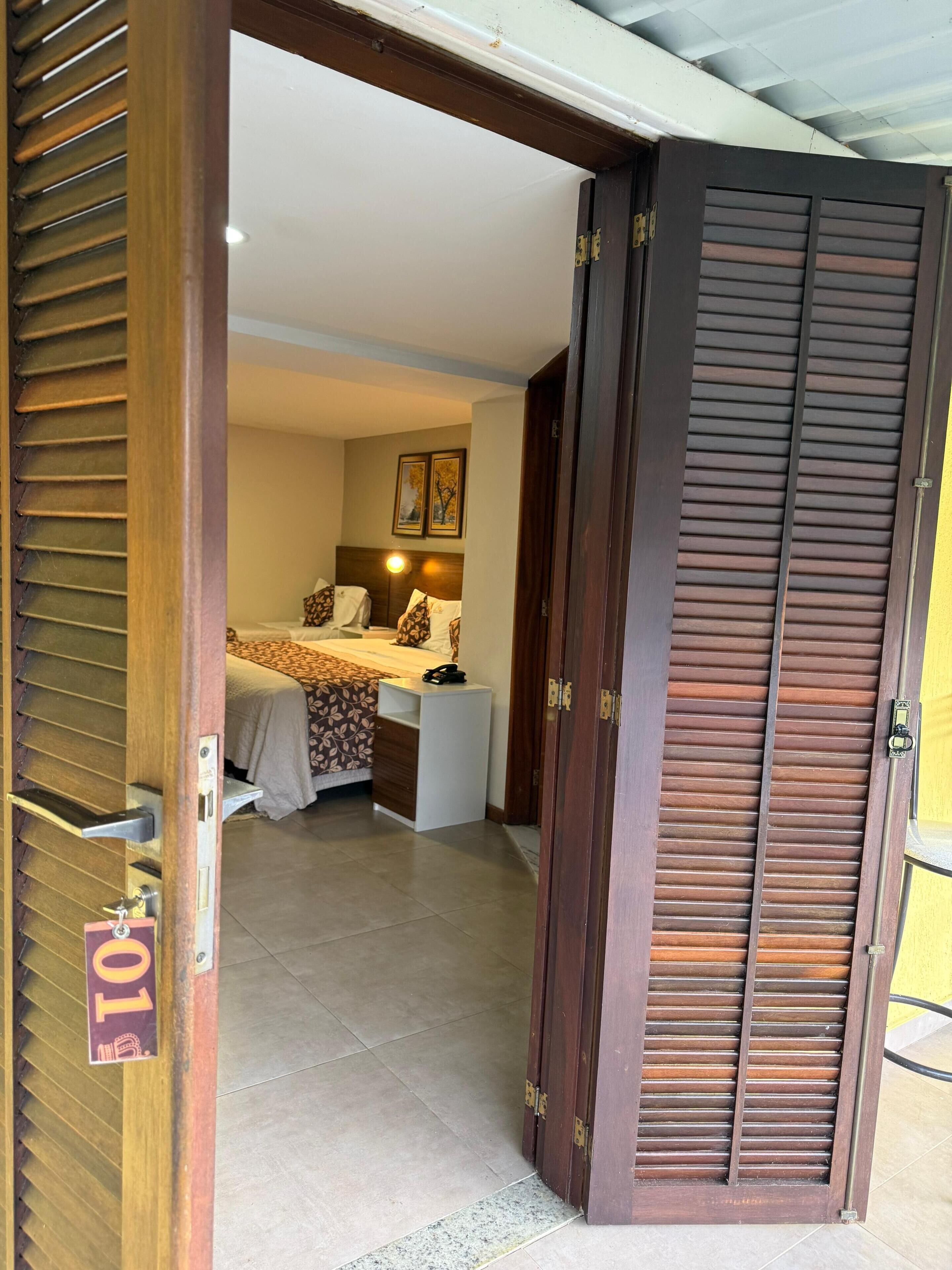 Une chambre d’hôtel avec un lit, une table de chevet et une porte dotée d’un volet en bois.