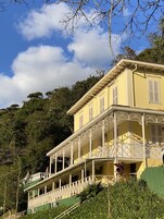A yellow building with a balcony, surrounded by greenery and trees.