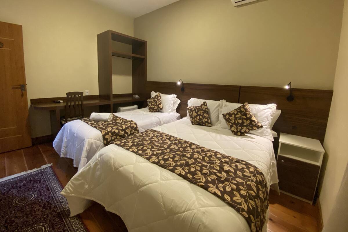 Quarto de hotel com duas camas, uma escrivaninha, uma cadeira, ar condicionado e um tapete.