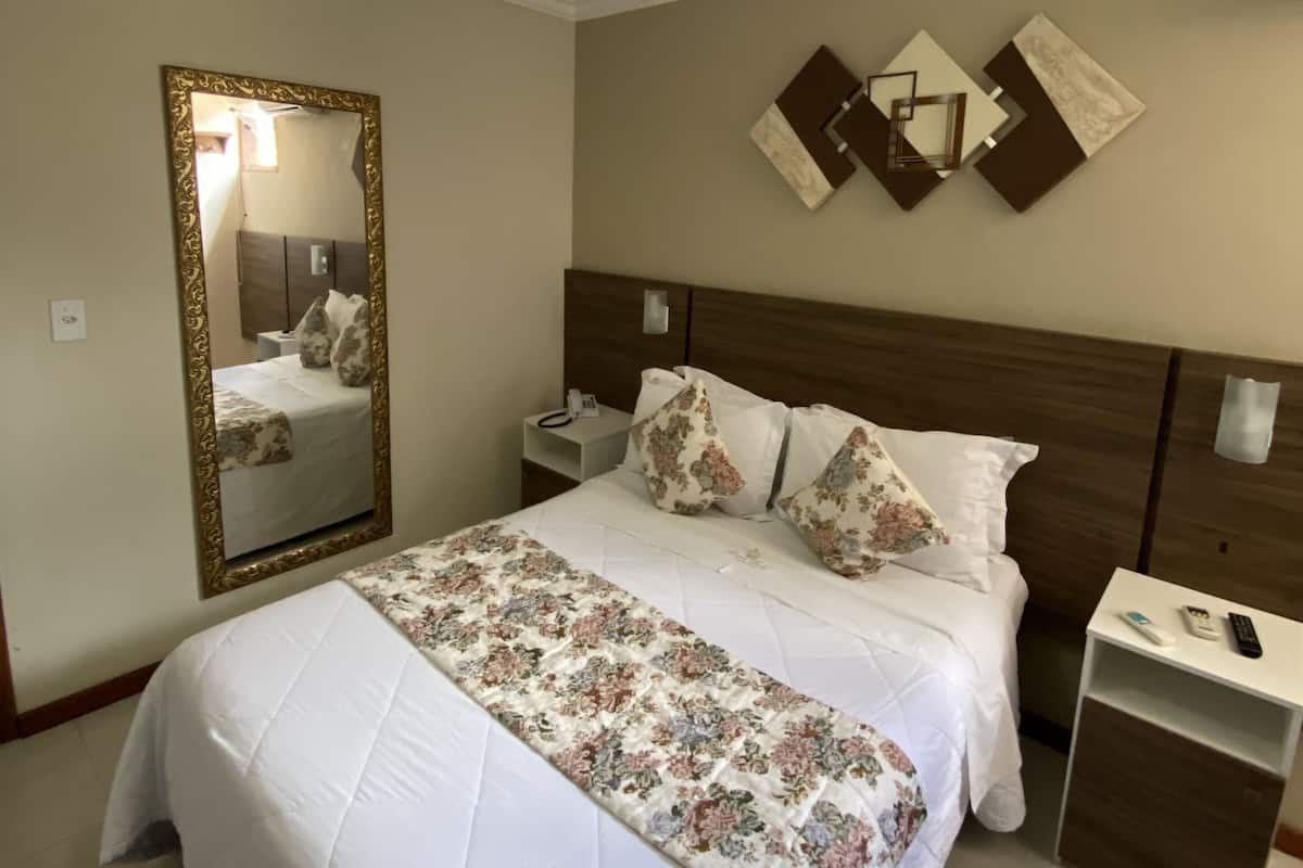 Quarto bem organizado com cama, mesa de cabeceira, espelho e ventilador de teto.