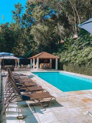 A swimming pool with lounge chairs, a gazebo, and lush greenery in the background. - Pousada Princesa Isabel - Visconde (Petrópolis)