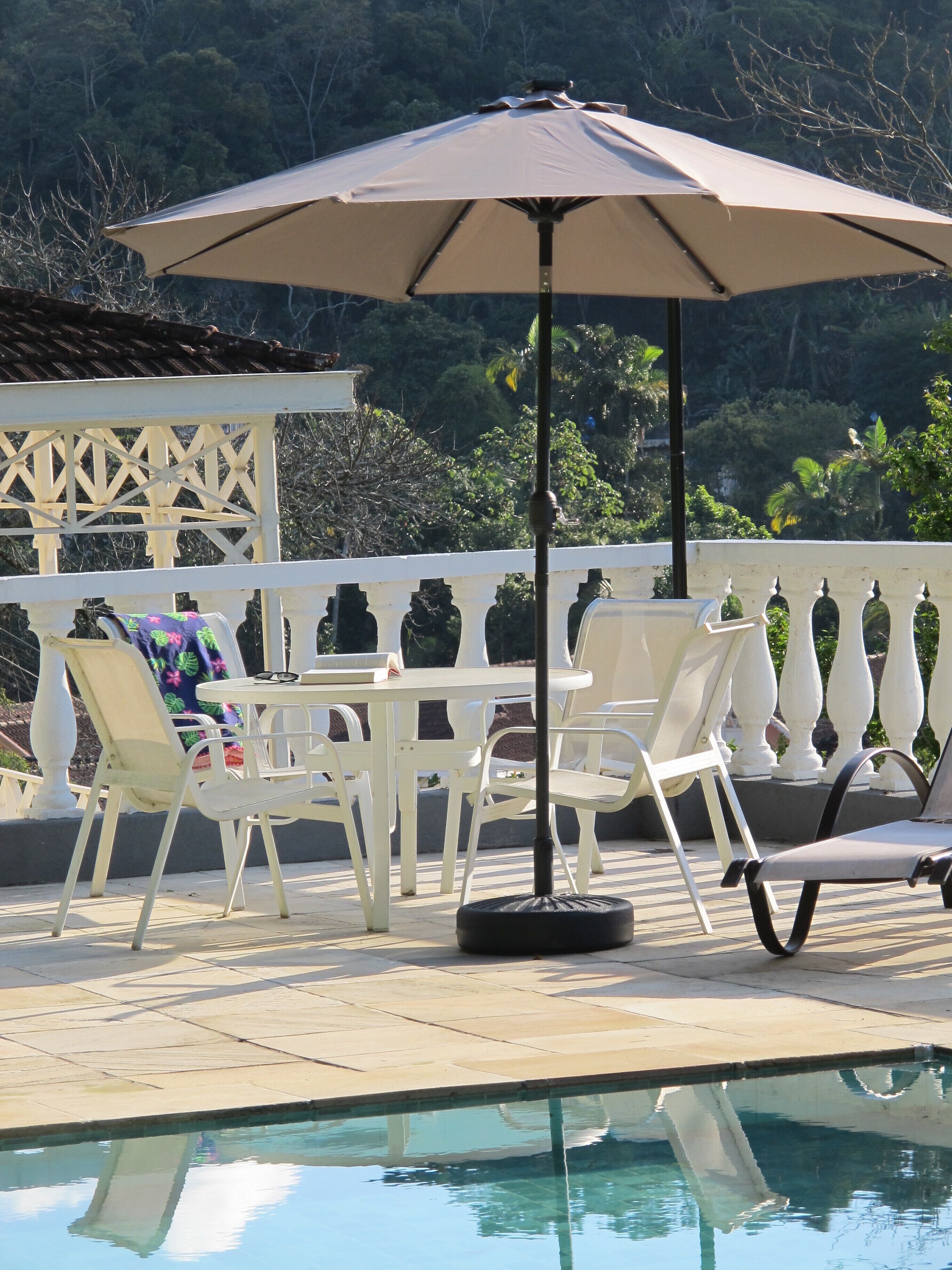 Un espace extérieur avec une piscine, une table et des chaises, un grand parasol et une clôture blanche.