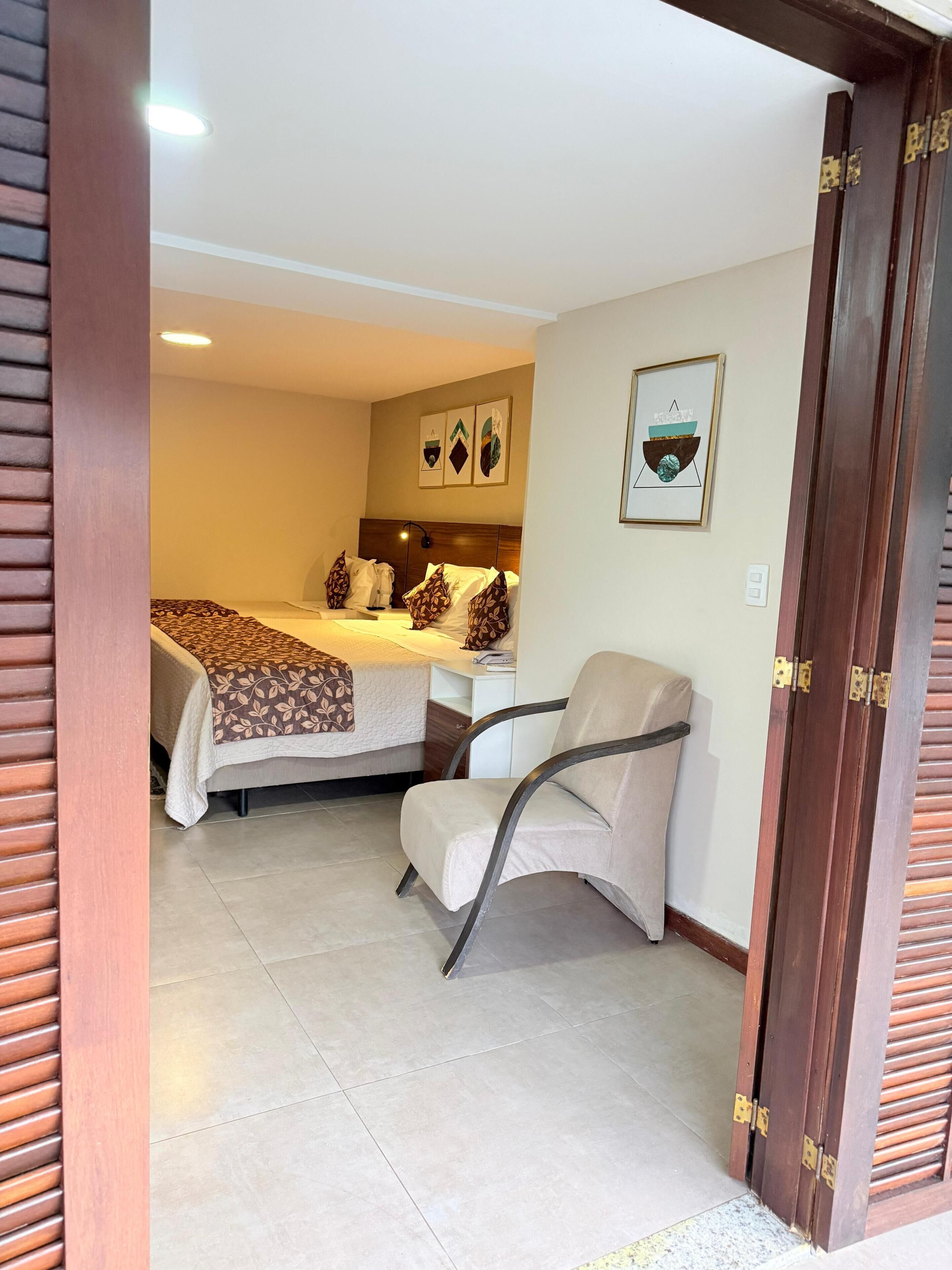 A hotel room with a bed, a chair, a nightstand, and a wall-mounted artwork.