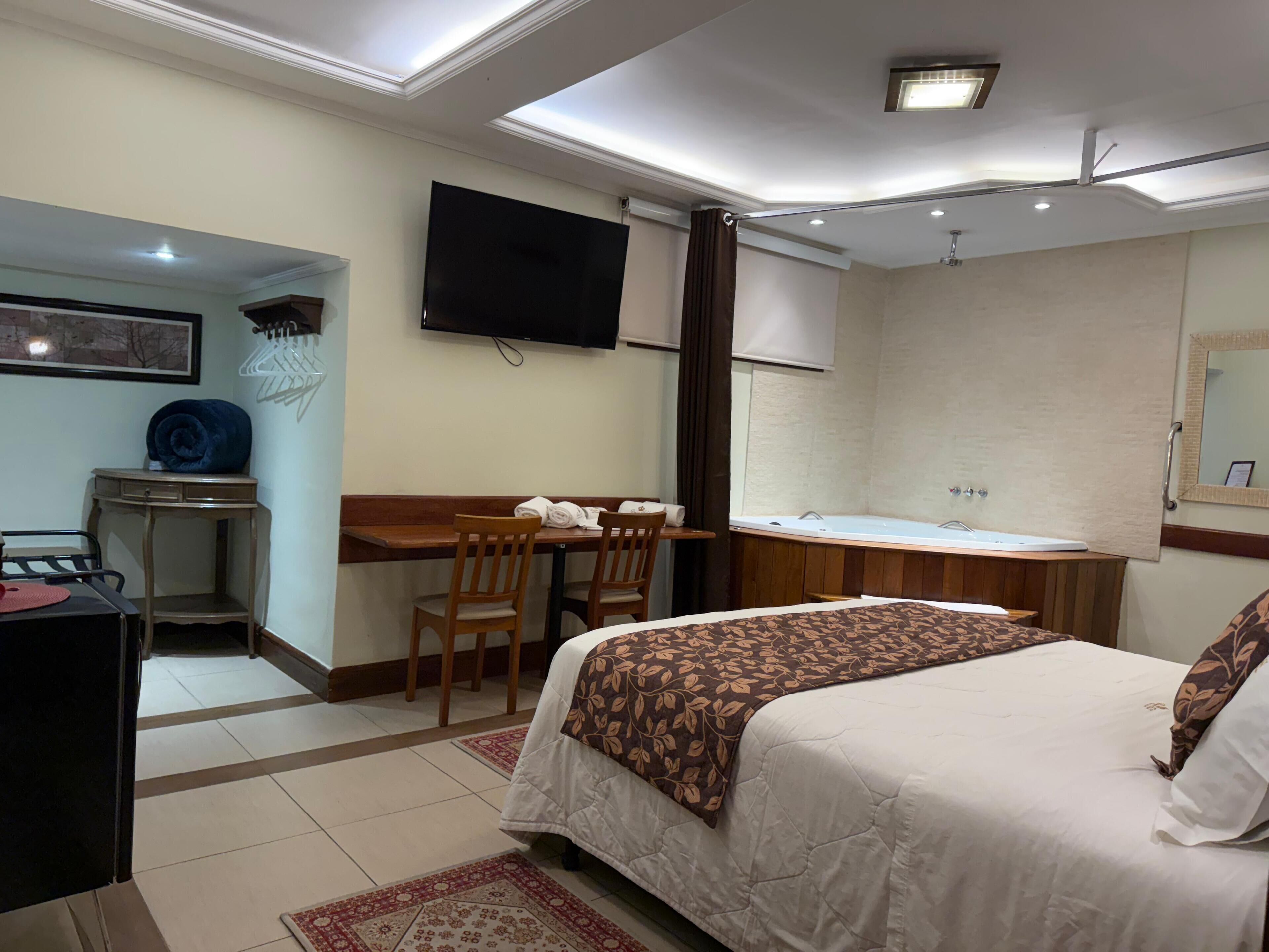 A hotel room with a bed, desk, chair, television, and a bathroom with a bathtub.