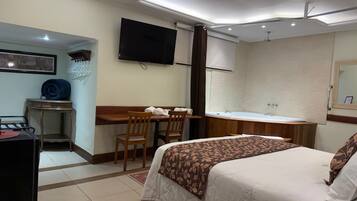 A hotel room with a bed, desk, chair, television, and a bathroom with a bathtub.