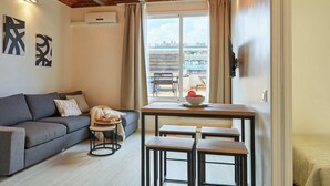 Una sala acogedora con un sofá gris, una mesita redonda con una bandeja y una ventana con vistas a edificios.