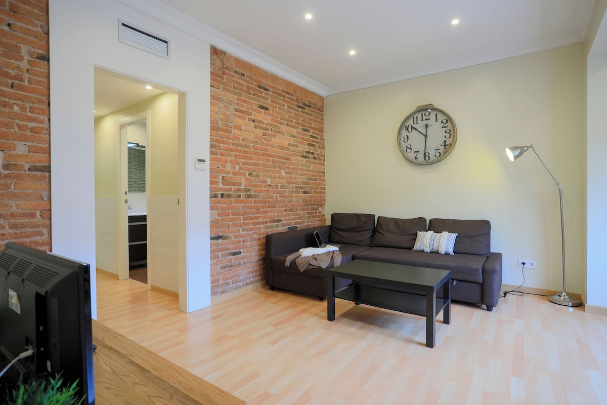 A modern living room with a brick accent wall, a sofa, a coffee table, a clock, and a floor lamp.