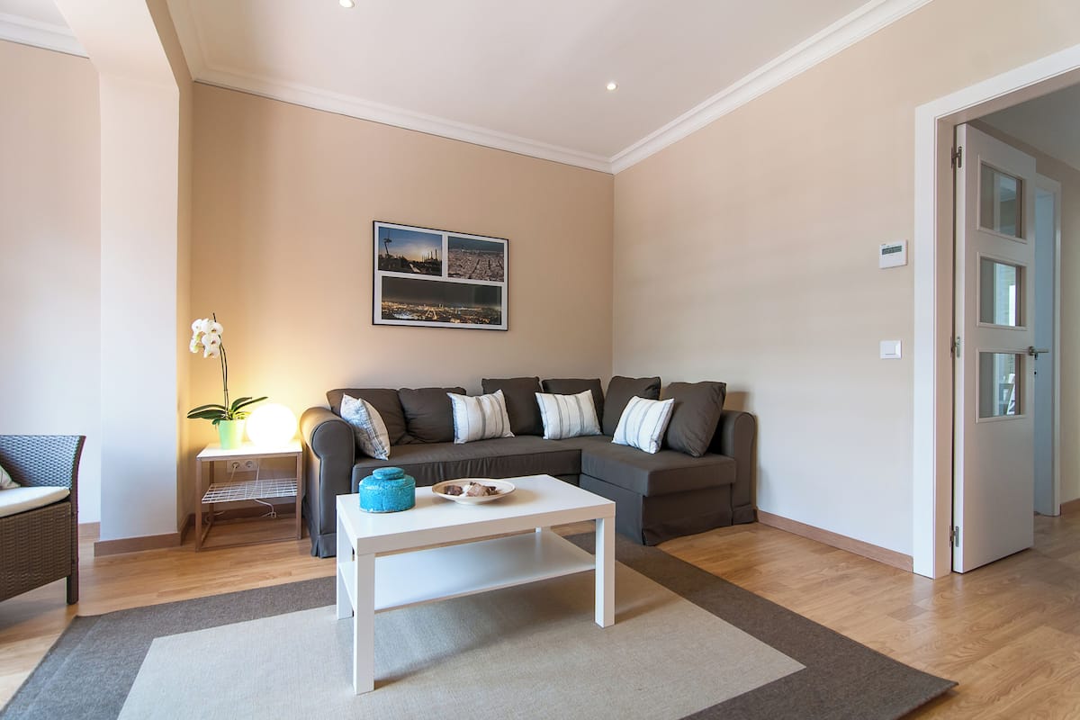 A living room with a sofa, a coffee table, a side table with a lamp, and a framed cityscape picture on the wall.