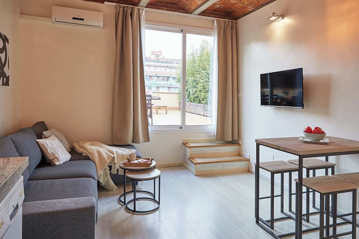 A modern living room with a grey sofa, a small round table, a wooden staircase, and a TV mounted on the wall.
