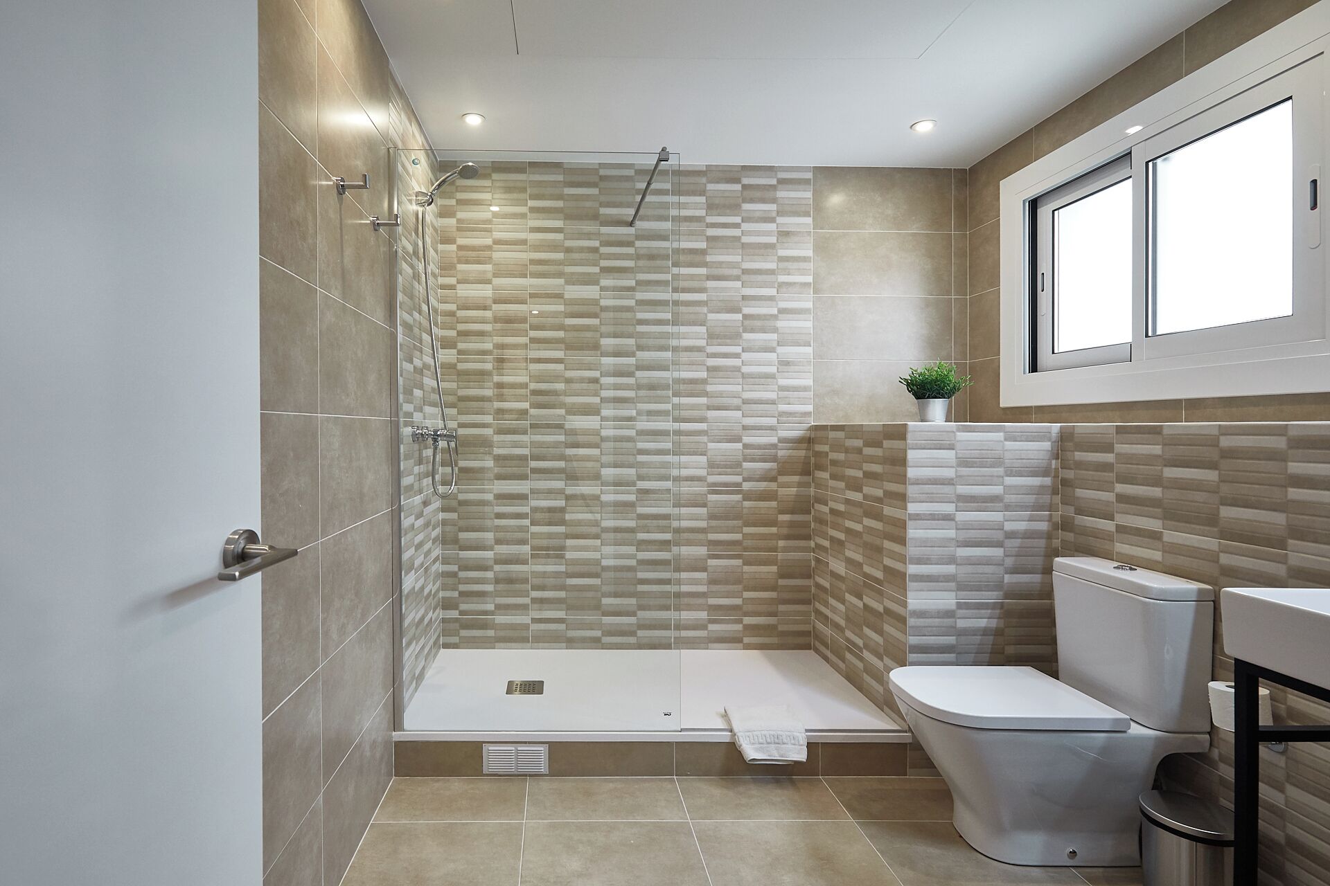 A modern bathroom with a shower, toilet, and a window above the sink.