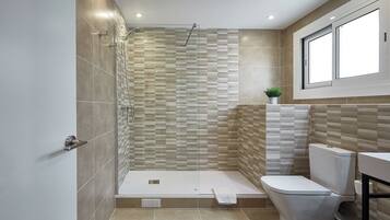 A modern bathroom with a shower, toilet, and a window above the sink.