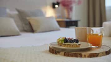 A neatly made bed with pillows, a small plate with a dessert, and a glass of orange juice on a wooden coaster.
