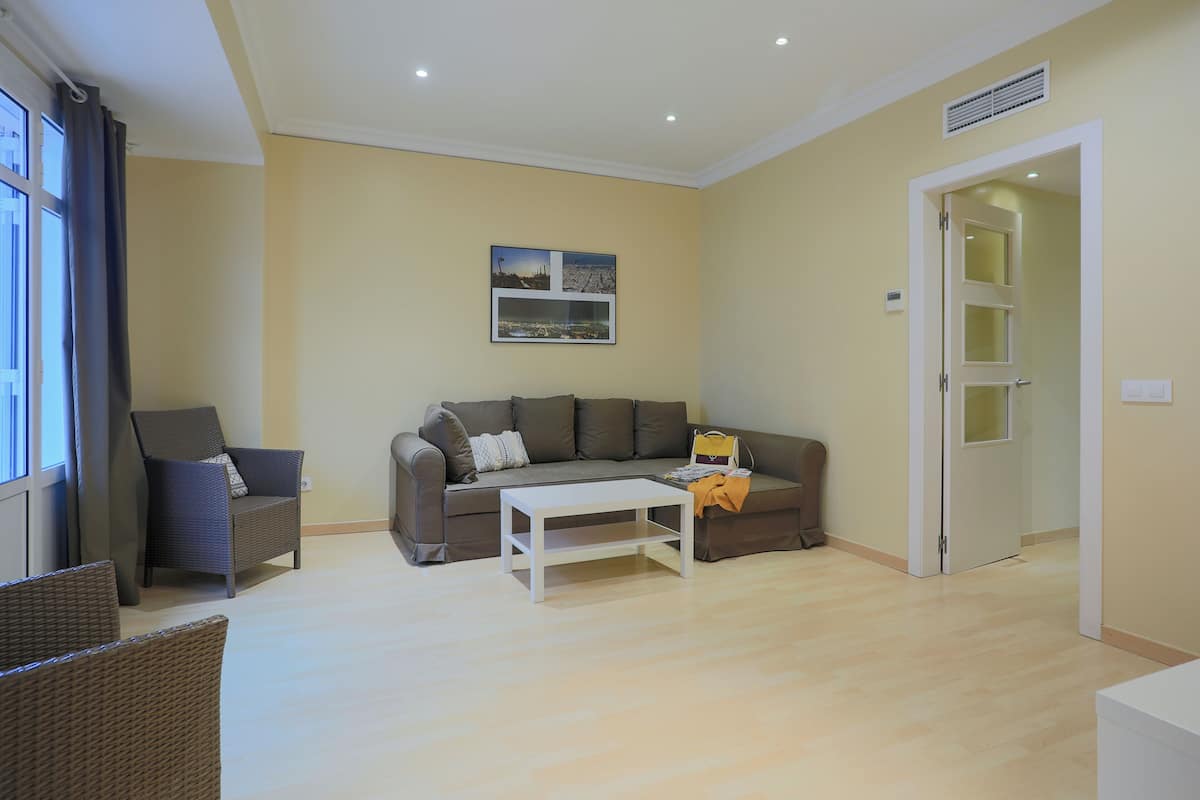A living room with a sofa, a coffee table, and a chair. There is a door and a window with curtains.