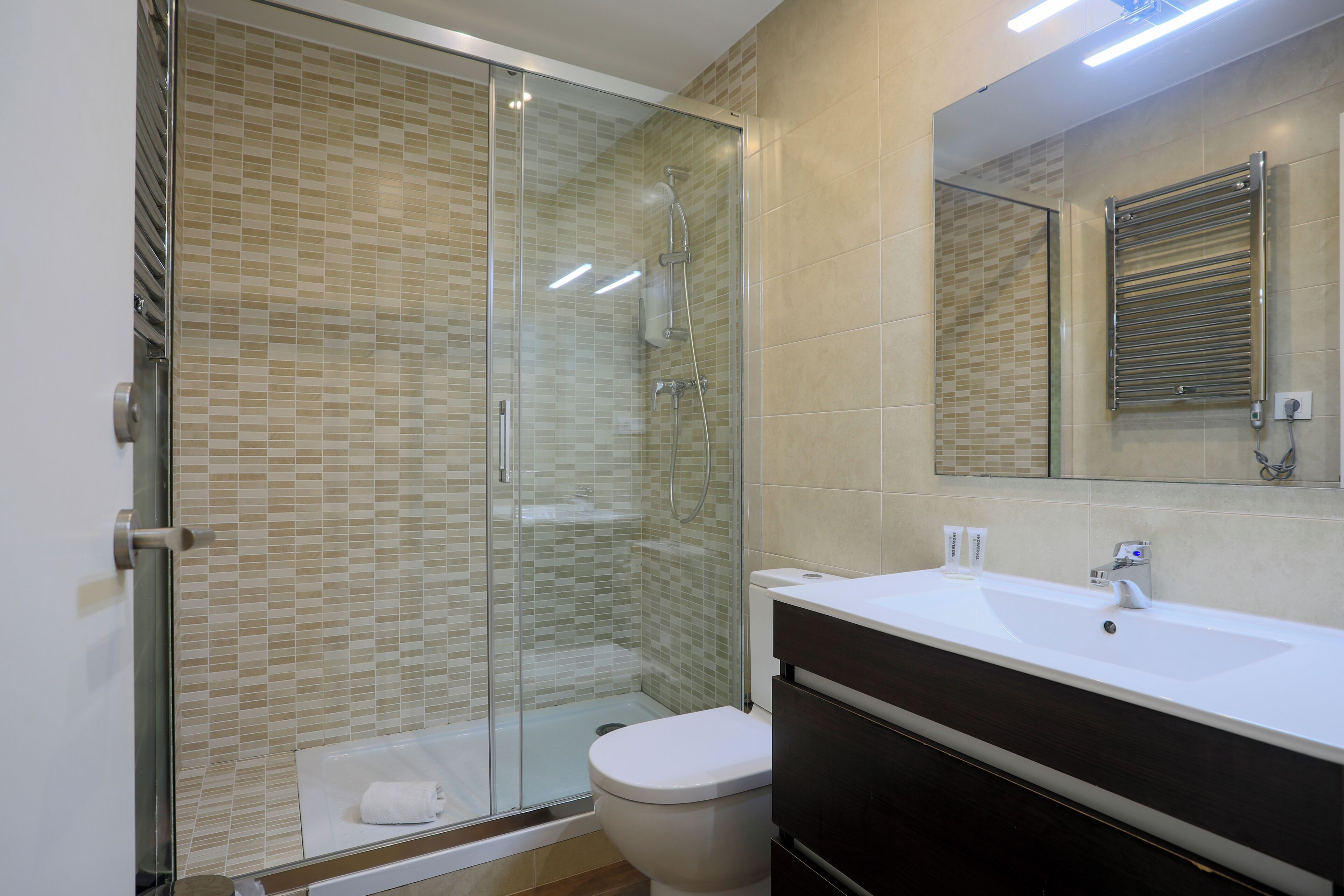 Un baño moderno con ducha cubierta de vidrio, lavamanos blanco y tocador oscuro.
