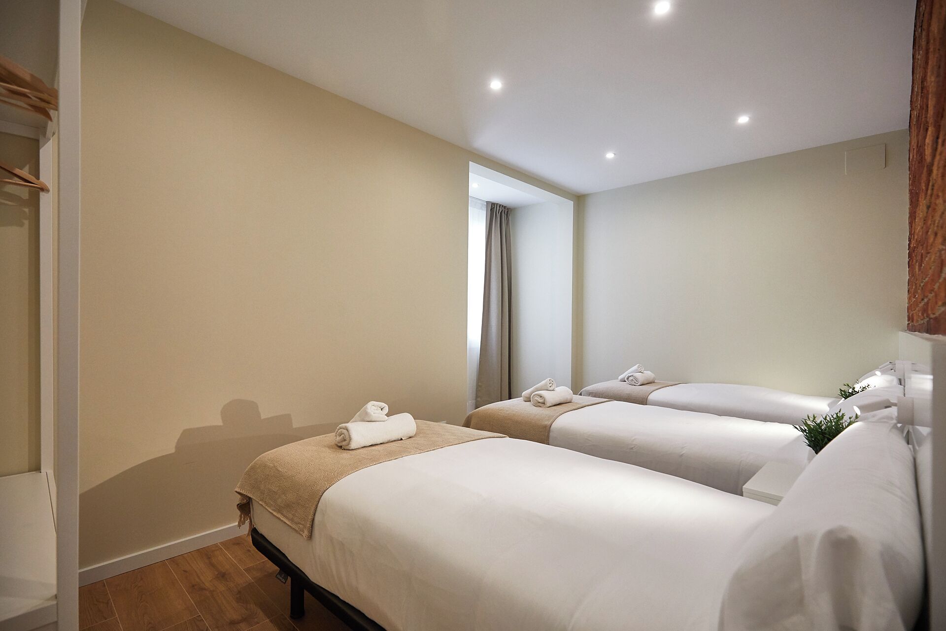 Een hotelkamer met twee bedden, een houten vloer, een grote spiegel en uitzicht op een gang.