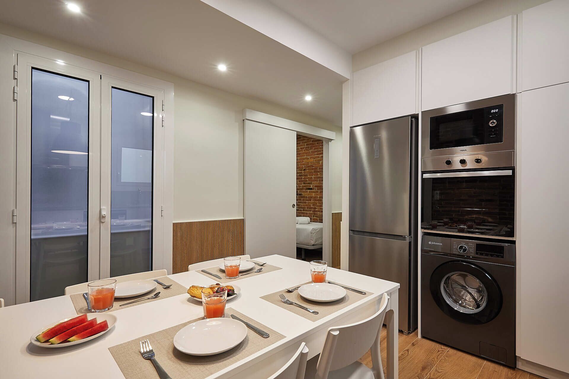 A modern kitchen with a dining area, featuring a stainless steel refrigerator, oven, and washing machine.