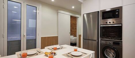 A modern kitchen with a dining area, featuring a stainless steel refrigerator, oven, and washing machine.