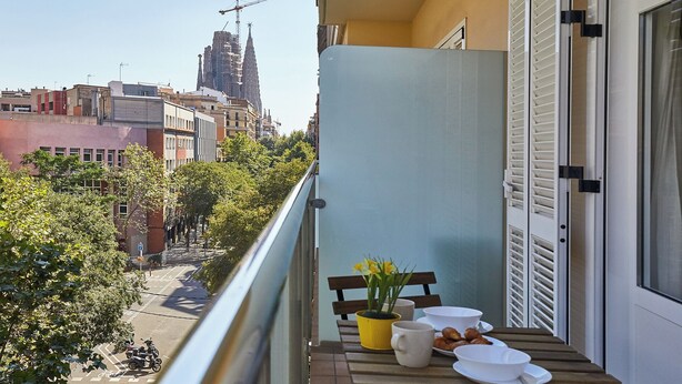 Un balcón con una mesa lista para el desayuno, con vistas a un paisaje urbano que incluye edificios y una grúa de construcción.