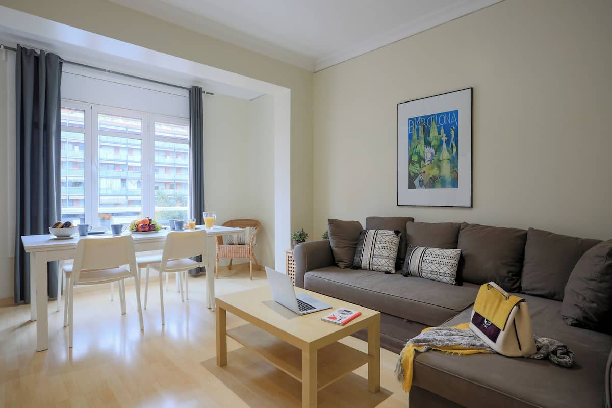 A modern living room with a sofa, a dining table with chairs, a laptop, and a framed picture on the wall.